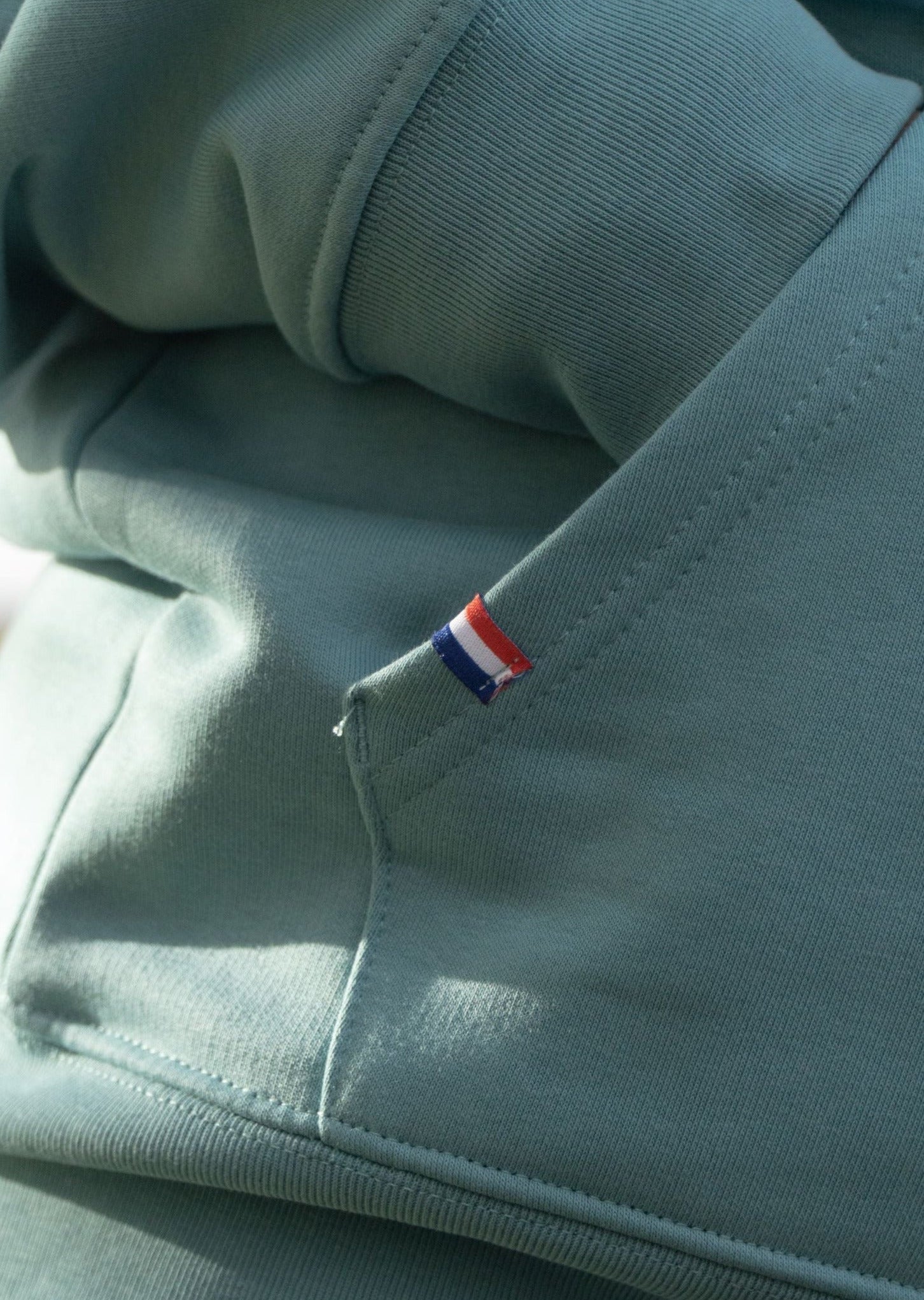 Hoodie de couleur vert brodé Mecton qualité premium et confort inégalable avec étiquette tissée aux couleurs du drapeau français. Sweatshirt épais pour rester au chaud, matière coton et polyester biologique issu du recyclage marin.